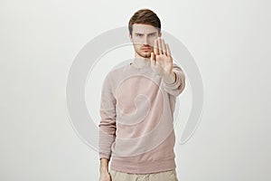 Portrait of calm serious young man with bristle stretching hand towards camera with stop or hold gesture, standing