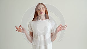 Portrait of calm young woman deeply breathing with closed eyes holding fingers in mudra om position, standing on white