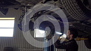 Portrait of car mechanic working with hammer under automobile in auto repair