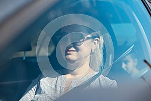 Portrait through car window, of woman driving. Wearing sunglasses.