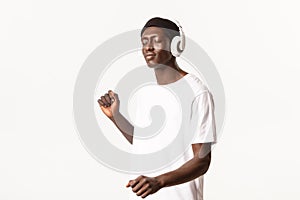 Portrait of carefree attractive african-american guy, close eyes and dancing while listening music in wireless