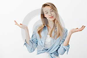 Portrait of carefree good-looking blonde in trendy outfit, raising spread palms and shrugging with positive happy smile