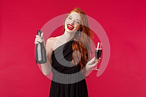 Portrait of carefree gorgeous redhead woman partying with friends, drinking from glass, holding bottle champagne and