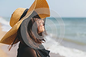 Portrait of carefree happy woman with windy hair in hat relaxing on sunny beach at sea. Summer vacation. Stylish calm young female