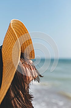 Portrait of carefree happy woman with windy hair in hat relaxing on sunny beach at sea. Summer vacation. Stylish calm young female