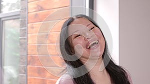 Portrait of carefree mature Asian woman laughing indoors