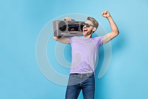 Portrait of carefree person hold boom box on shoulder fist up open mouth smile isolated on blue color background