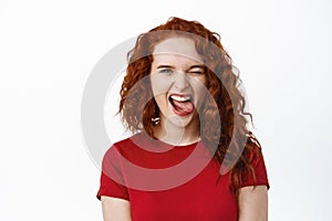 Portrait of carefree young teen ginger girl making positive funny faces, showing tongue and smiling, winking at camera