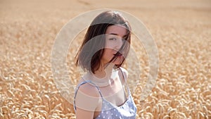 Portrait of carefree young woman looking at camera in ripe wheat field at sunset