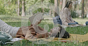 Portrait of carefree young woman reading book lying on lawn in park enjoying modern literature