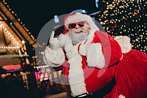 Portrait of careless brutal fat aged santa carry gifts sack hand fingers show heavy metal symbol evening tree lights