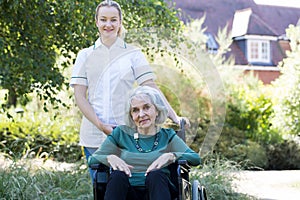 Portrait Of Carer Pushing Senior Woman In Wheelchair Outside Home