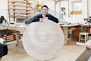 Portrait of a carpenter standing in his woodwork studio carpenter workshop. The man holds a wooden round board for the text.