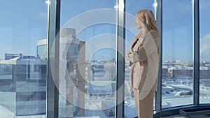 Portrait of casual businesswoman standing in front of window on high floor of office building. Woman enjoying outside