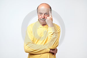 Portrait of casual mature man in yellow shirt thinking and looking puzzled