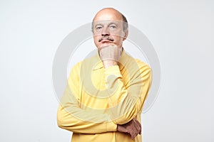 Portrait of casual mature man in yellow shirt thinking and looking puzzled
