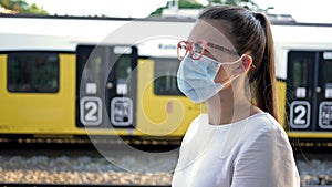 Portrait of casual woman waiting train with protective mask at face. Travel, tourism during the COVID-19 epidemic.