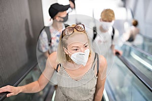 Portrait of casual yound woman uses escalators in the department store wearing protective mask as protection against