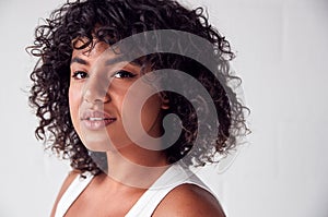 Portrait Of Casually Dressed Woman In Vest Top Standing Against White Brick Studio Wall