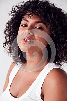 Portrait Of Casually Dressed Woman In Vest Top Standing Against White Brick Studio Wall