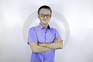 Portrait of a casually dressed young Asian man standing confidently with his arms crossed against a grey wall.