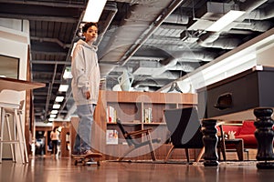 Portrait Of Casually Dressed Young Businesswoman With Skateboard Standing In Open Plan Workplace