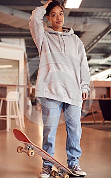 Portrait Of Casually Dressed Young Businesswoman With Skateboard Standing In Open Plan Workplace