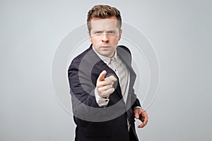 Portrait of caucasian angry young man in suit pointing finger at you