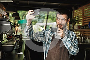 Portrait of caucasian barista man taking selfie photo while working in street cafe or coffeehouse outdoor