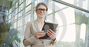 Portrait of the Caucasian beautiful businesswoman, taping on the tablet computer, smiling to the camera and posing on