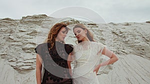 Portrait of Caucasian beautiful young females in white and black dresses back to back and smiling to camera or looking