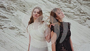 Portrait of Caucasian beautiful young females in white and black dresses back to back and smiling to camera or looking