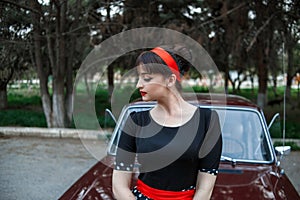 Portrait of a Caucasian beautiful young girl in a black vintage dress, posing near a vintage car