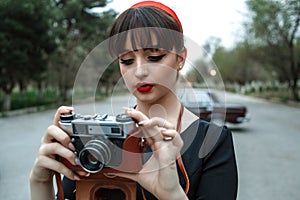 Portrait of Caucasian beautiful young girl in black vintage dress posing with vintage camera in hands