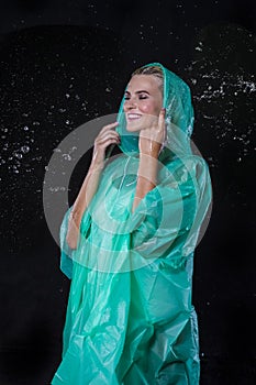 Portrait of Caucasian Blond Female in Green Raincoat Posing Under The Water Drops Against Black Background