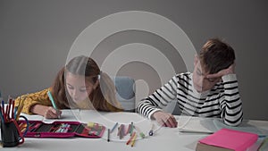 Portrait of a Caucasian boy throwing pen on the table. His diligent female classmate looking at him surprisingly