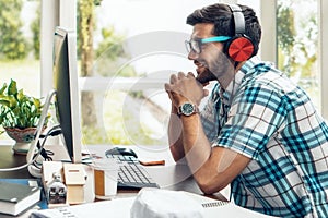 Portrait of caucasian businessman sitting at working desk with computer smiling and listening to music with headset at home office