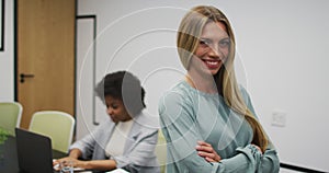 Portrait of caucasian businesswoman smiling in office, with colleague working in background