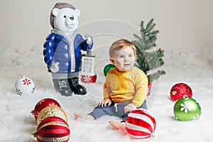 Child baby in yellow sweater clothes sitting on white fluffy rug celebrating Christmas or New Year