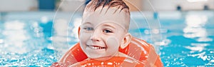 Caucasian child in swimming pool. Preschool boy  training to float with red circle ring in water.