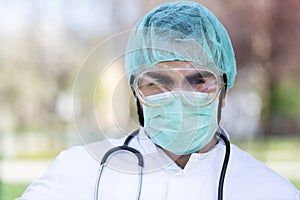 Portrait of a Caucasian Doctor male with mask, scrub cap holding a stethoscope in the garden