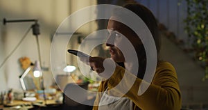 Portrait of caucasian female jeweller in workshop wearing apron, using smartphone, talking