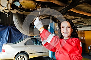 Portrait of a Caucasian female mechanic in a red uniform standing under the car bottom for inspecting in the garage. A woman