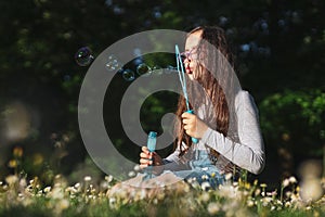 Portrait of a caucasian girl blowing soap bubbles while sitting in a flower meadow in a park