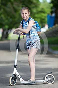 Portrait of caucasian girl in full length standing near kick scooter on an asphalt track