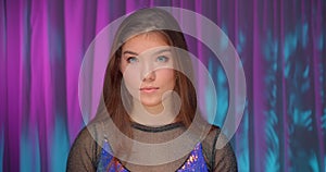 Portrait of caucasian girl in neon light dress purple background confident serious look