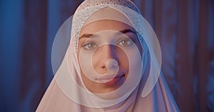 Portrait of caucasian girl in white hijab neon light look at the camera temptation night eye makeup blue background