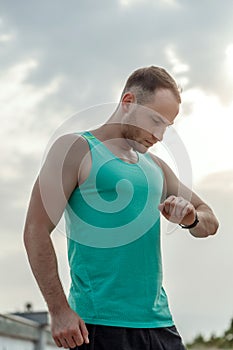 Portrait of Caucasian guy in azure t-shirt looking at fitness tracker readings after or before Jogging