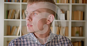 Portrait of caucasian librarian watching sidewards turns watching at camera with serious glance on bookshelves