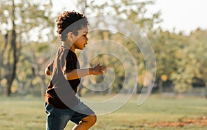 Portrait of Caucasian little white curly hair boy, running and playing with happiness and running in park at evening summer time